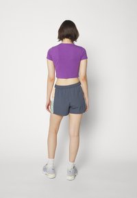 Violet trumpas marškinėliai derinami su tamsiai pilkomis šortais, puoštais pastelinių spalvų akcentais. Modelis vilki šviesiai violetinius sportbačius su baltais kojin rytas.