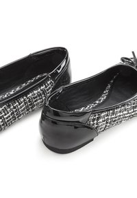 Ballerine in vernice nera e tweed bianco e nero con punta arrotondata e un piccolo dettaglio a fiocco sul davanti. Design con suola piatta.