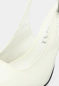 Λευκά παπούτσια με ψηλό τακούνι και γυαλιστερό φινίρισμα, με σχεδιασμό χαμηλής κοπής, λεία υφή και μαύρες σόλες.