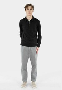 Pullover nero a maniche lunghe con colletto zip, abbinato a jeans grigi chiari e scarpe chiare. Tessuto liscio, design semplice.