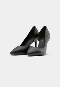 Escarpins noirs à talons hauts avec un bout pointu et une finition en cuir lisse, présentant un dos courbé et une texture brillante.