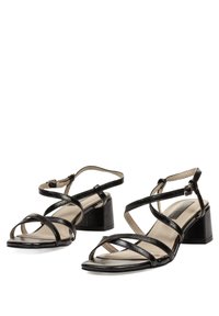 Sandalias de tacón negras con tiras, con un tacón bloque, que presentan tiras delgadas y una suela plana. El material superior tiene un acabado brillante.