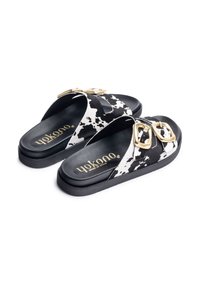 Black and white cow print sandals made of synthetic material, featuring gold-tone hardware accents and a cushioned footbed for comfort.