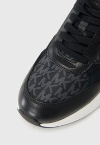 Sorte sneakers med en glatt lær tåhette og et mønstret syntetisk overdeler med grå bokstaver. Snøringer og teksturerte detaljer i matchende farge.