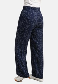 Navy wide-leg pants featuring a white leaf pattern, elastic waistband, and side pockets. Smooth texture with casual athletic shoes.
