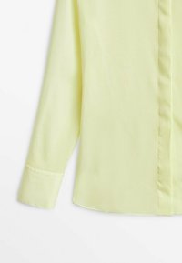 Camicia a maniche lunghe gialla chiara realizzata in tessuto morbido. Presenta una chiusura a bottoni frontale e un taglio dritto con collo e polsini standard.