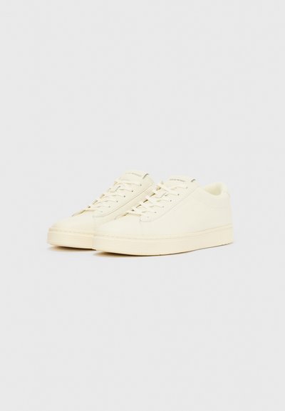 Ténis off-white com parte superior em tecido liso, bico redondo, atacadores planos e sola grossa texturada. Design minimalista sem marca visível.