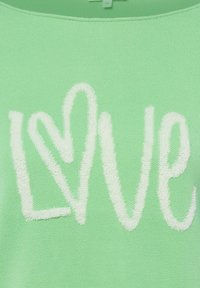 Groen textiel met witte, gestructureerde letters die het woord "LOVE" vormen, waarbij een hartvorm is geïntegreerd in de letter "O".