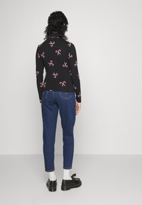 Svart långärmad tröja med röda godisstänger i mönster, kombinerad med blå denim tapered jeans och svarta skor med tofsar.