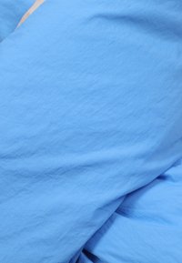 Svetlomodrá tkanina s pokrčenou štruktúrou, która obsahuje jemné záhyby a hladké oblasti, čím vytvára vrstvený vzhľad bez výrazných vzorov.