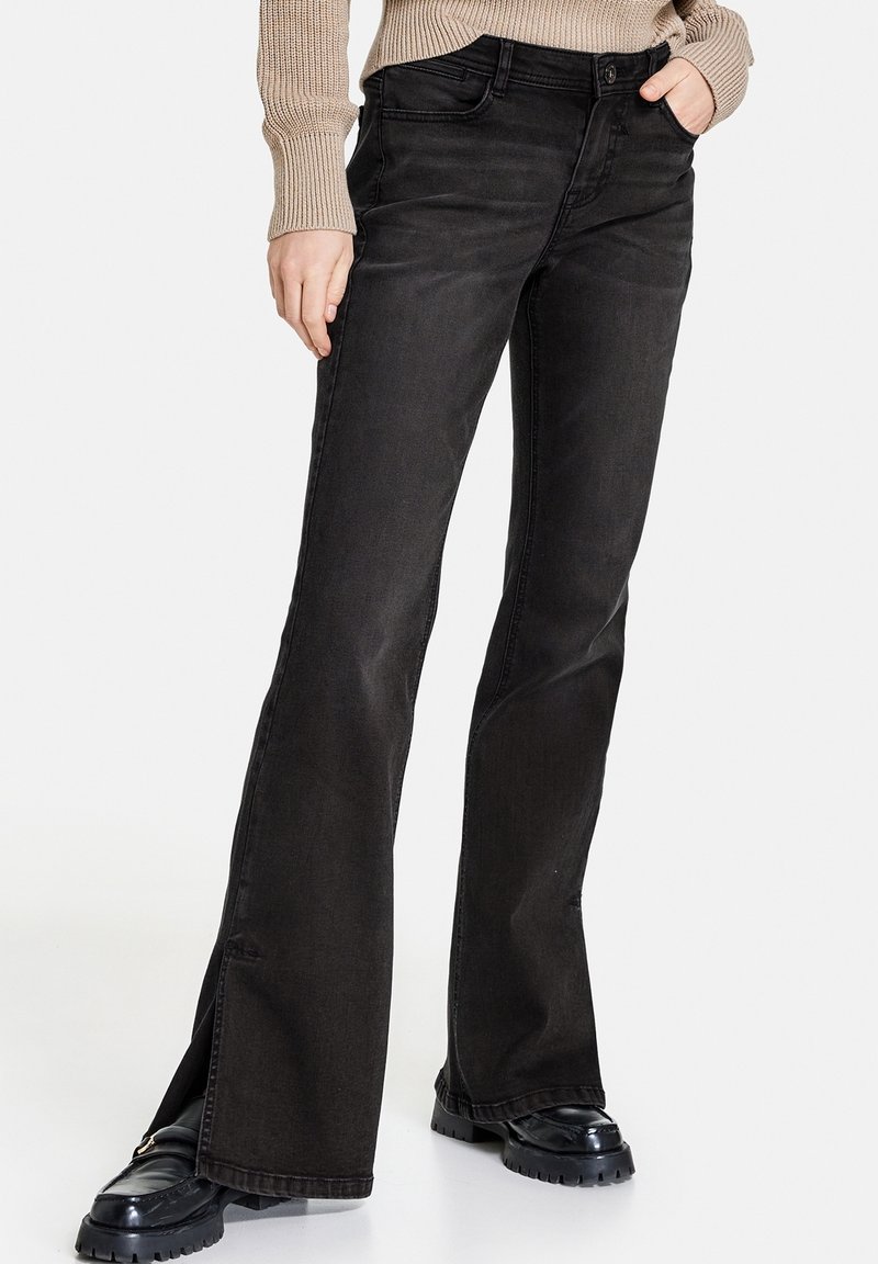 Pantalones vaqueros acampanados negros con una cintura de altura media, fabricados en denim. Presentan un bolsillo frontal, un ligero desgaste y detalles de abertura en la parte inferior.
