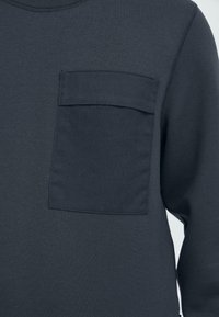 Donkergrijze sweatshirt met een gestructureerde stof, een ronde halslijn en een opgestikte zak aan de linkerkant van de borst. Gladde textuur met minimale details.