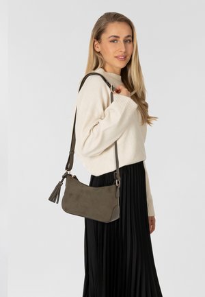 Olivgrünes Wildleder-Crossbody-Bag mit verstellbarem Riemen, Quastenakzent und abgerundeten Kanten, präsentiert vor einem neutralen Hintergrund.