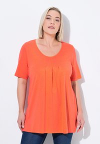 Světlý oranžový top s krátkým rukávem a výstřihem ve tvaru lopatky, se sklady na přední straně. Vyrobeno z měkkého, lehkého materiálu.