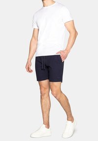 Hvid bomulds t-shirt kombineret med marineblå shorts med snoretræk. Modellen har hvide sneakers på. Enkel, afslappet påklædning.