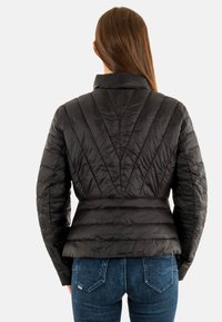 Giacca a vento nera con design trapuntato, caratterizzata da un colletto alto e vita aderente. Texture liscia con tessuto lucido.