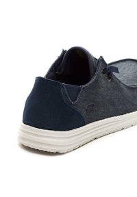 Sneaker blu scuro con tomaia in suede e tessuto texturizzato, suola bianca e piccolo dettaglio del logo. Presenta fori per i lacci e una forma arrotondata.