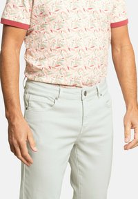 Jeans verde menta claros de corte ajustado con bolsillos delanteros. Combinados con una camisa de manga corta, estampada en tonos pastel y acentos rojos.