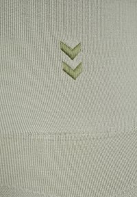 Ljusgrön ribbad tyg med en slät yta, med två nedåtriktade gröna pilar broderade i nederdelen av mitten.