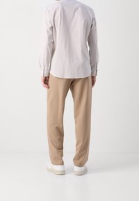 Vaaleansävyinen raidallinen nappipaita, yhdistettynä väljään beigeen housuihin ja valkoisiin lenkkareihin. Paidassa on pitkät hihat ja napilliset kalvosimet.