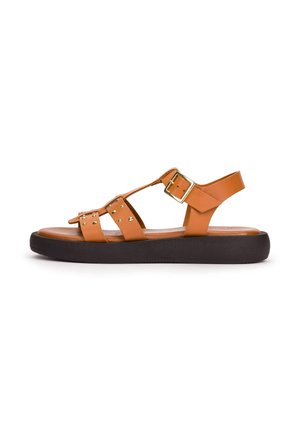 Sandale en cuir marron avec des clous dorés, une bride réglable avec boucle dorée et une semelle noire épaisse vue de côté sur fond blanc.