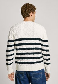 Pull rayé blanc et bleu marine avec une texture en tricot torsadé, un col rond et des poignets et un ourlet côtelés. La vue arrière révèle des motifs complexes.