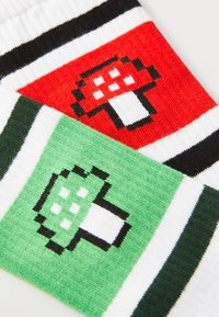 Calzini di cotone colorati con design di funghi pixelati in rosso e verde, arricchiti da strisce bianche e nere per un tocco in più.