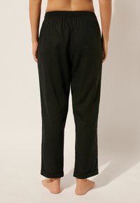 Pantalons noirs amples avec une taille élastique. Le tissu semble doux avec des ourlets enroulés aux chevilles. Pas de motifs ni de matériel visibles.