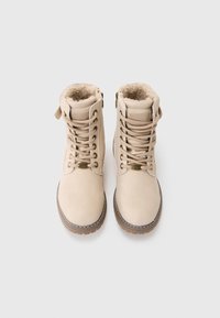 Botines beige con cordones en la parte delantera, punta redonda y forro de piel de pelo. Presentan una suela de goma resistente y costuras decorativas. Cremallera en el lateral.