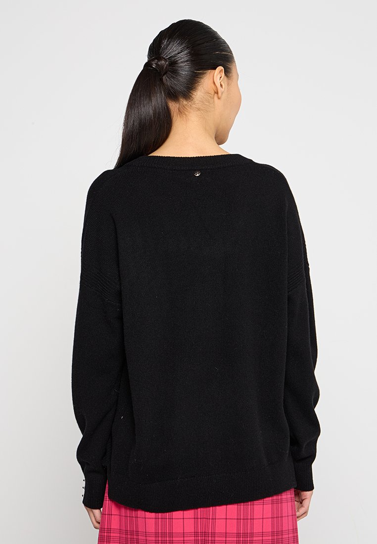 Maglione nero lavorato a maglia con vestibilità rilassata, polsini a coste e un piccolo bottone dettagliato sul retro del collo. Texture morbida e design semplice.