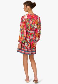 Florales Kleid mit lebhaften pinken und grünen Mustern, langen Ärmeln, tailliertem Schnitt und einem gestuften Rock mit dekorativem Saum.