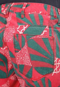 Rood en groen gemusterde shorts met een gedurfde bladdesign, voorzien van een achterzak en gestikte details. Gemaakt van een katoenmix.