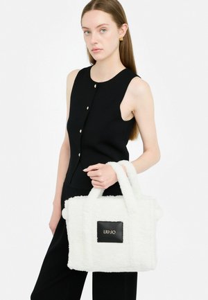 Borsa a tracolla bianca e soffice con due manici corti, caratterizzata da un'etichetta logo rettangolare nera. Modella che indossa un top senza maniche nero.