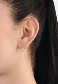 Orecchini a cerchio dorati con un design a forma di cuore decorato con piccoli cristalli trasparenti, esposti all'orecchio di un modello.