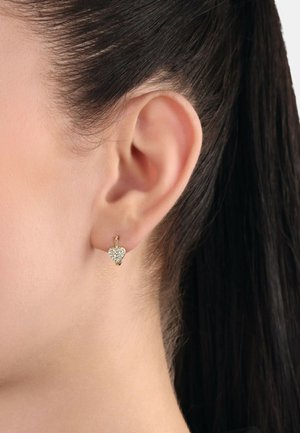 Pendientes de aro dorados con un diseño en forma de corazón adornado con pequeños cristales transparentes, mostrados en la oreja de un modelo.