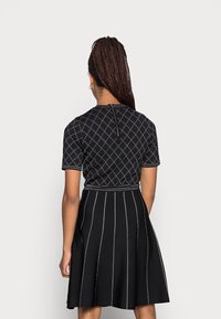 Robe noire à manches courtes, motif en losanges, surpiqûres blanches contrastantes, corsage ajusté et jupe évasée. Fermeture éclair au dos.