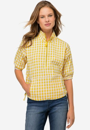 Giacca pullover a scacchi gialla e bianca con maniche corte, zip frontale a metà e tasche laterali. Presenta polsini elasticizzati e orlo regolabile.