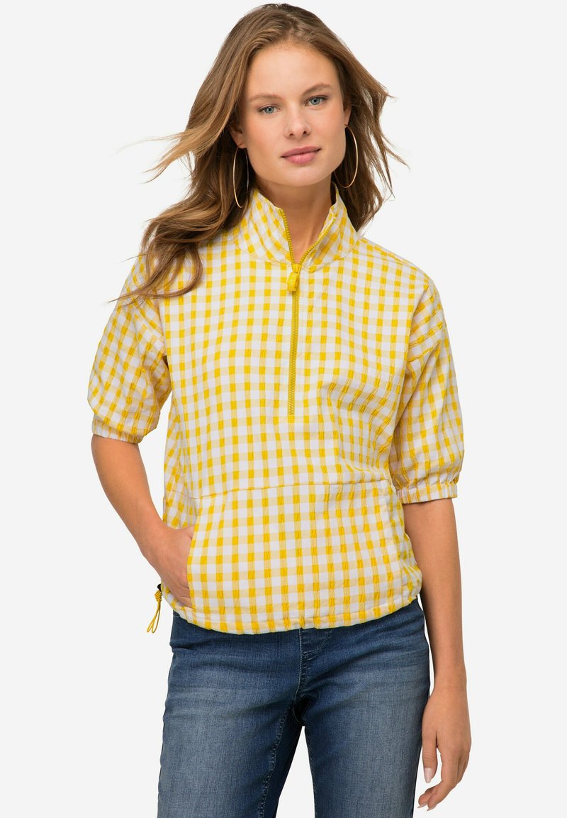 Giacca pullover a scacchi gialla e bianca con maniche corte, zip frontale a metà e tasche laterali. Presenta polsini elasticizzati e orlo regolabile.