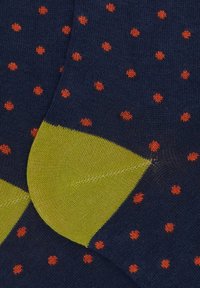Calzini blu navy con piccoli pois arancioni e toppe sul tallone di un vivace verde, vista ravvicinata della trama a maglia.