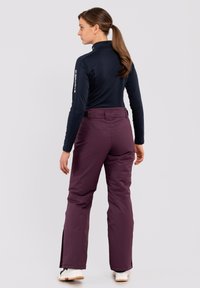 Marineblauwe top met lange mouwen, gecombineerd met wijnrode broek, met een getailleerde taille, ontspannen pijpen en ritsen bij de enkels. Glad van structuur en lichtgewicht.