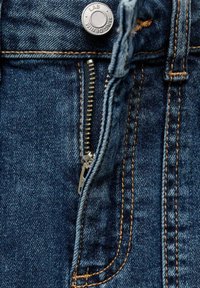 Jeans iz džinsa z modrim teksturiranim blagom, ki vključujejo kovinske gumbne zaponke, zadrgo in kontrastno rumeno šivanje ob šivih.