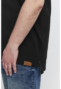 Must karvane t-särk, millel on külgsisselõige, ja hemil pruun nahklabel. Kandmiseks sinised teksased.