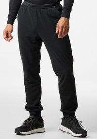 Zwarte fleece joggerbroeken met een aansluitende tailleband, taps toelopende broekspijpen en een gladde textuur. Draagt zwarte sportschoenen.