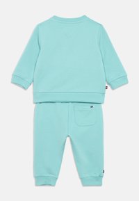 Hele sinine puuvillane treeningkostüüm, millel on ümar kaelus ja soonikkoes mansetid. Topp on ühetooniline, samas kui pükstel on tagaküljel tasku detail.