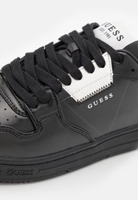 Sneaker in pelle nera con lacci neri e dettagli bianchi. Presenta un logo in rilievo, punta perforata e suola testurizzata per una migliore aderenza.