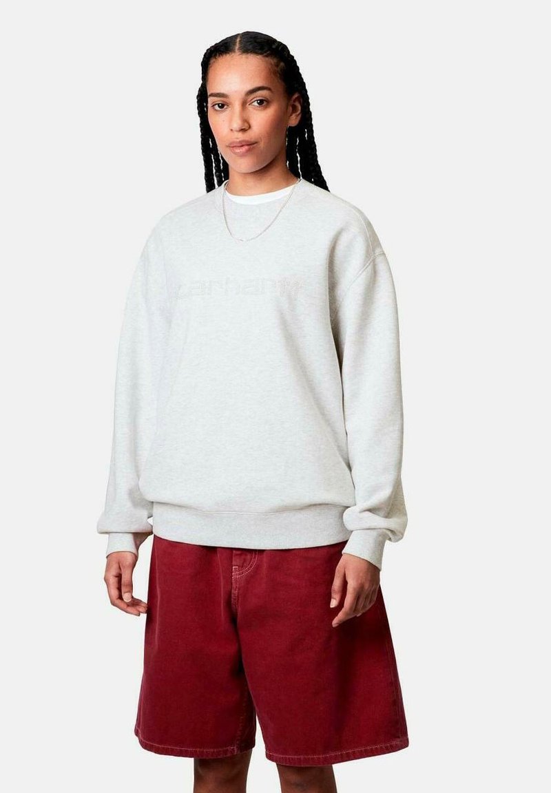 Sudadera gris con hombros caídos y puños de canalé, combinada con pantalones cortos de mezclilla rojos. Presenta un sutil logo en la parte delantera.