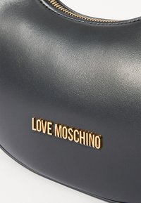 Črna usnjena torbica s ukrivljeno obliko, ki vsebuje zlat logotip "LOVE MOSCHINO" in zlate podrobnosti z zadrgo. Gladka tekstura in moderen dizajn.