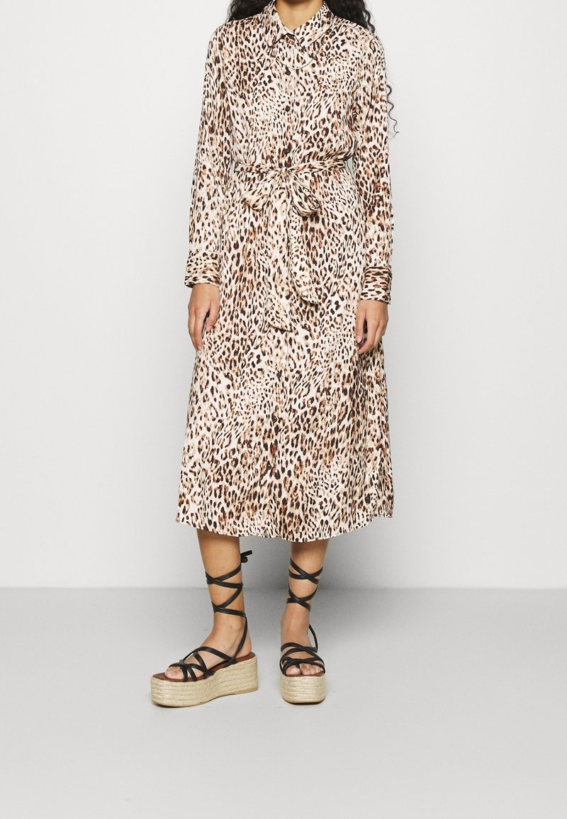 Frau trägt ein langärmeliges Midi-Kleid mit Leopardenmuster, einem gebundenen Taillengürtel und schwarze, riemchenbesetzte Plateausandalen.