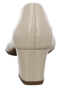 Beige lakovaná kožená bota na podpatku s kulatou špičkou a středním blokovým podpatkem. Švy podél zadního švu a hladký povrch.