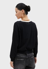 Black sweatshirt with a relaxed fit, contrasting cream collar, and small accent detail at the back. Paired with distressed dark jeans.